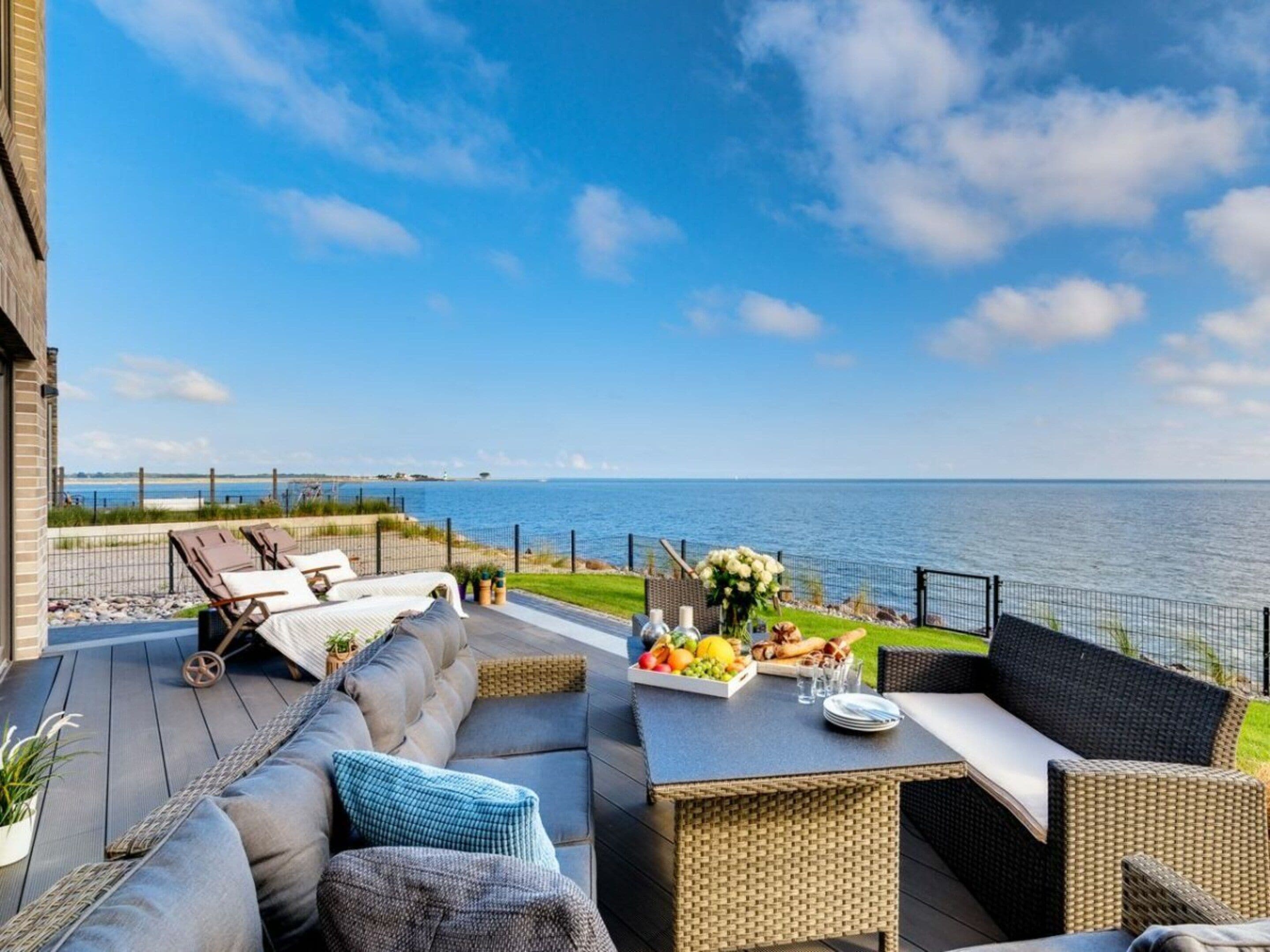 A deck with outdoor seating, a table with a fruit platter, and a view of the sea.
