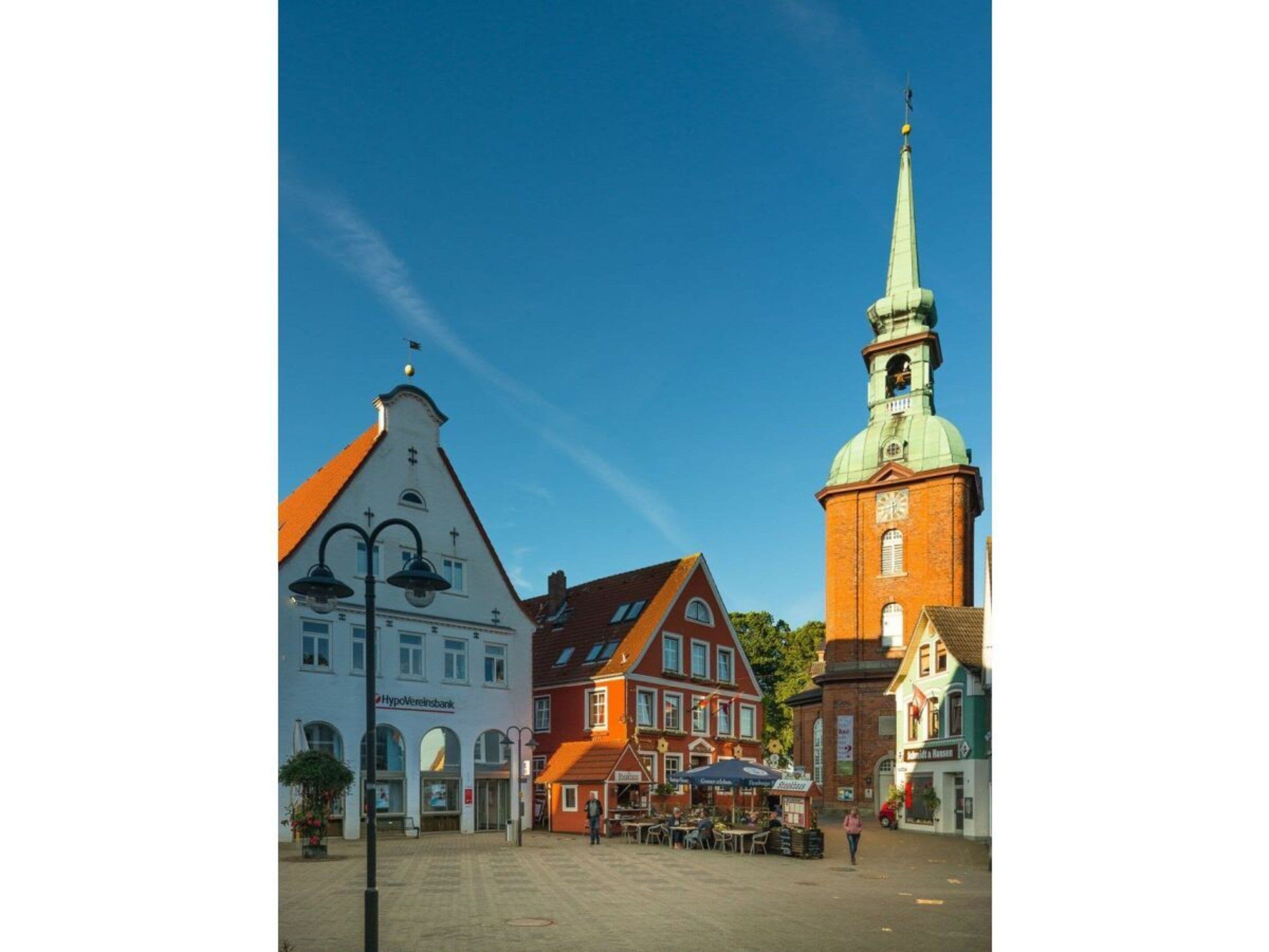 A town square with historic buildings, a church tower, and outdoor seating areas.