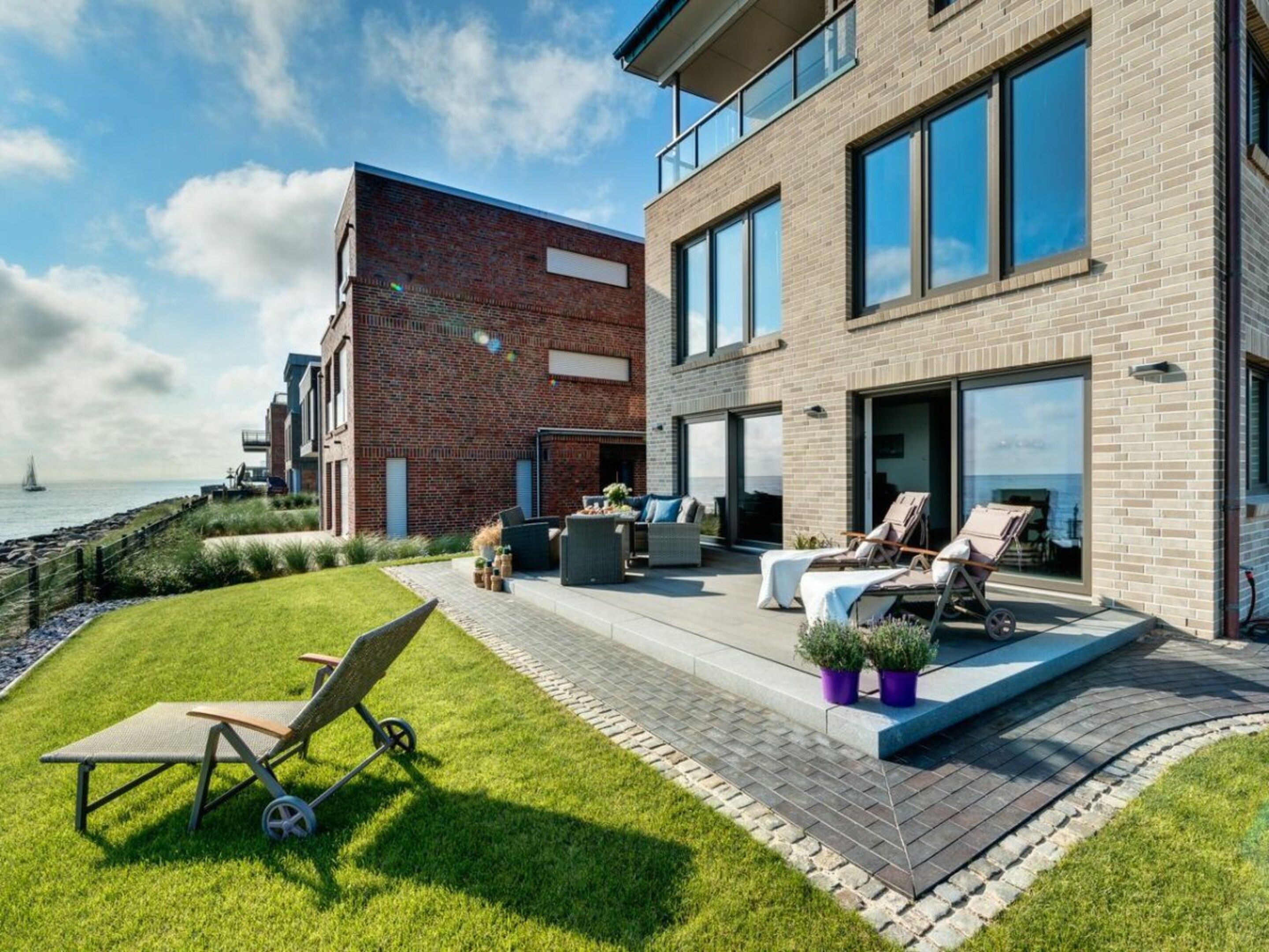 A modern two-story house with a patio area featuring outdoor furniture and a grassy lawn.
