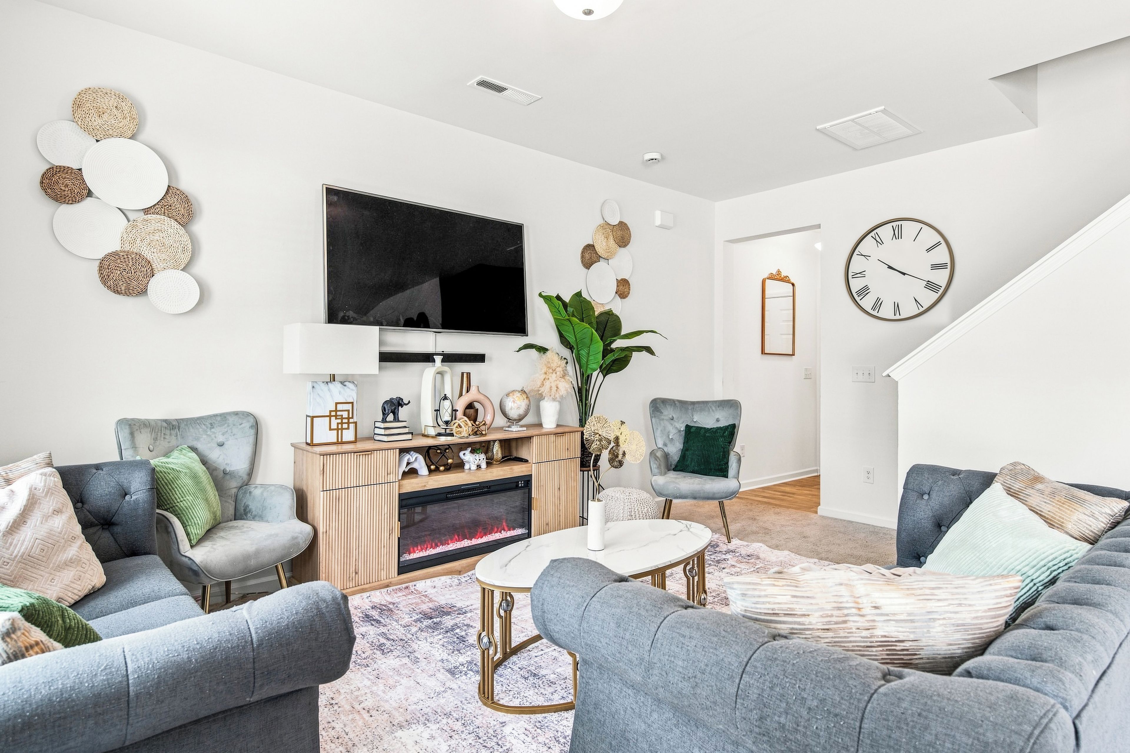 A modern living room with grey sofas, a flat-screen TV, a wooden entertainment unit, and a large clock on the wall.