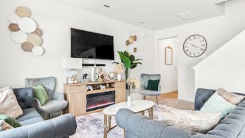A modern living room with grey sofas, a flat-screen TV, a wooden entertainment unit, and a large clock on the wall.