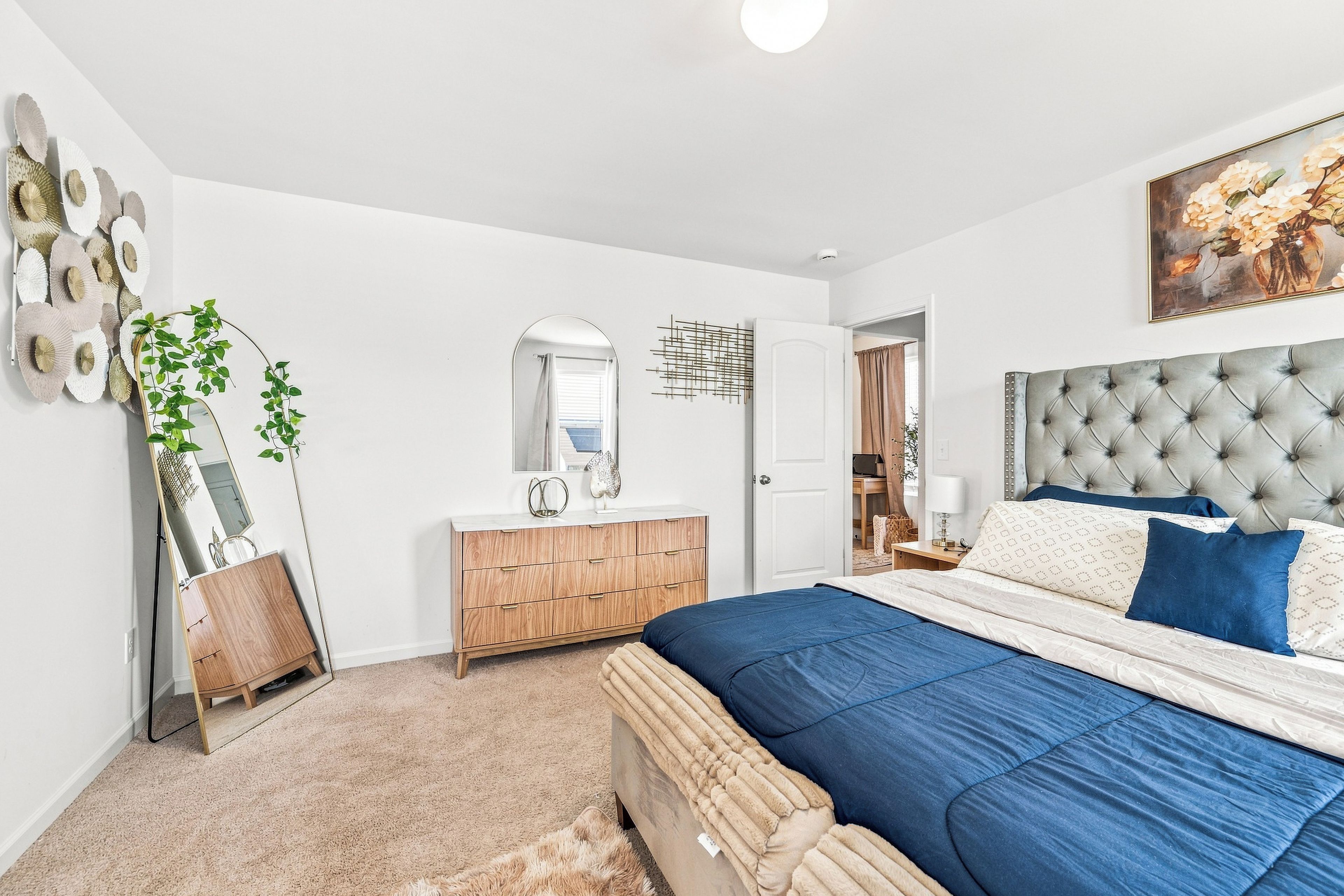 A bedroom with a bed, dresser, mirror, and a door leading to another room.