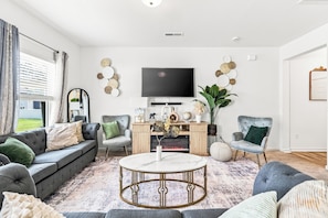 Una sala moderna con un sofá gris, dos sillones, una mesa de centro y un televisor de pantalla plana montado en la pared.