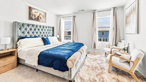 A bedroom with a large bed, a nightstand, a chair, and a window with curtains. - The Velvet Stay (Granite Quarry)