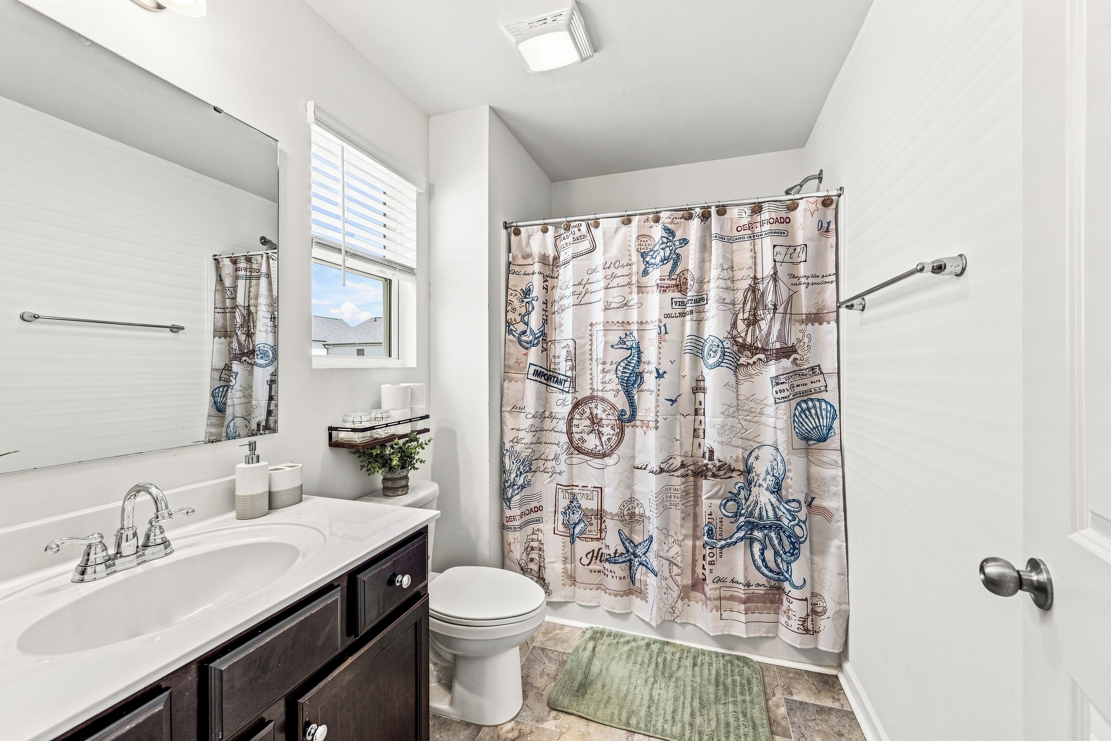 Une salle de bain avec un lavabo blanc, des toilettes et un rideau de douche orné de motifs marins.