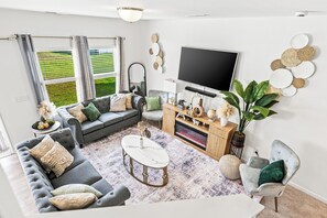 Una sala de estar moderna con un sofá gris, una mesa de centro blanca y un televisor de pantalla plana montado en la pared.