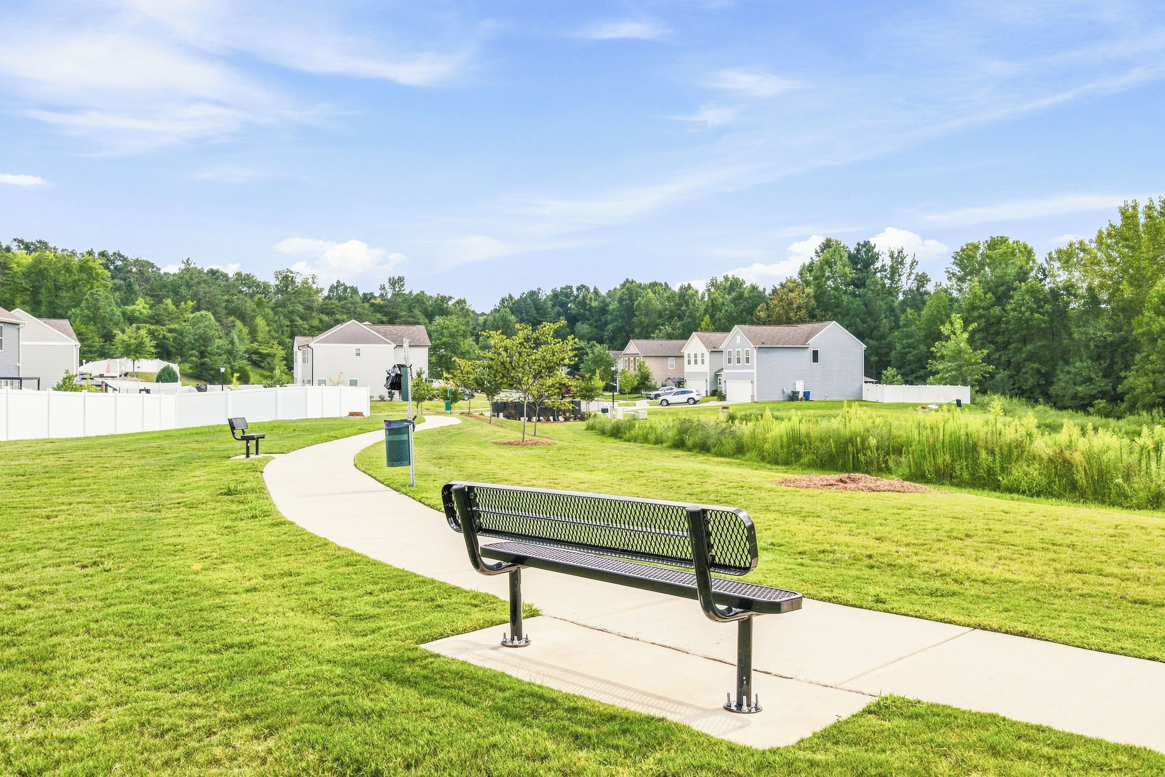 Un parc avec un banc, un sentier et des maisons en arrière-plan.