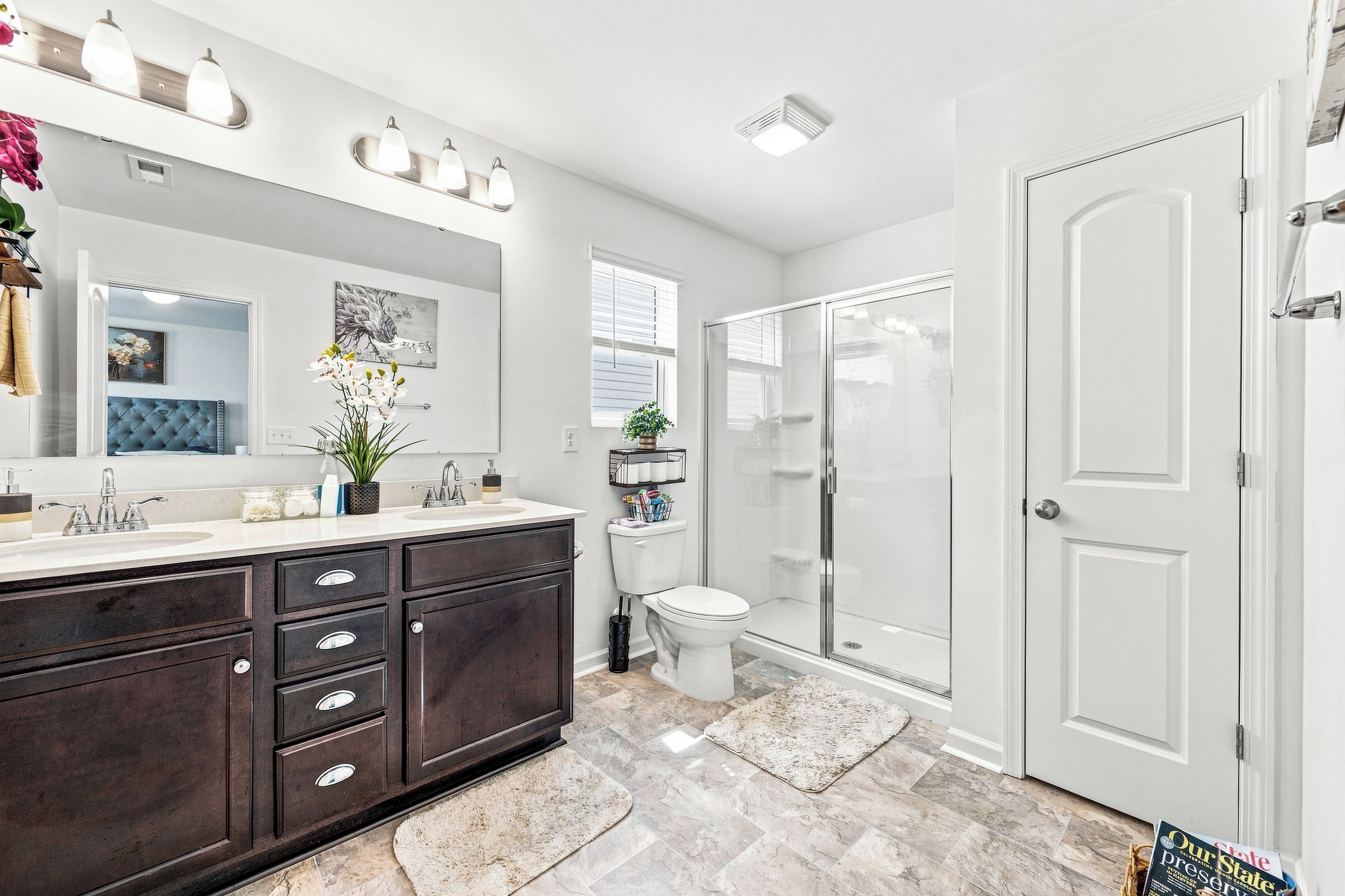 A modern bathroom with a dark wood vanity, a large mirror, a shower enclosure, and a white door.