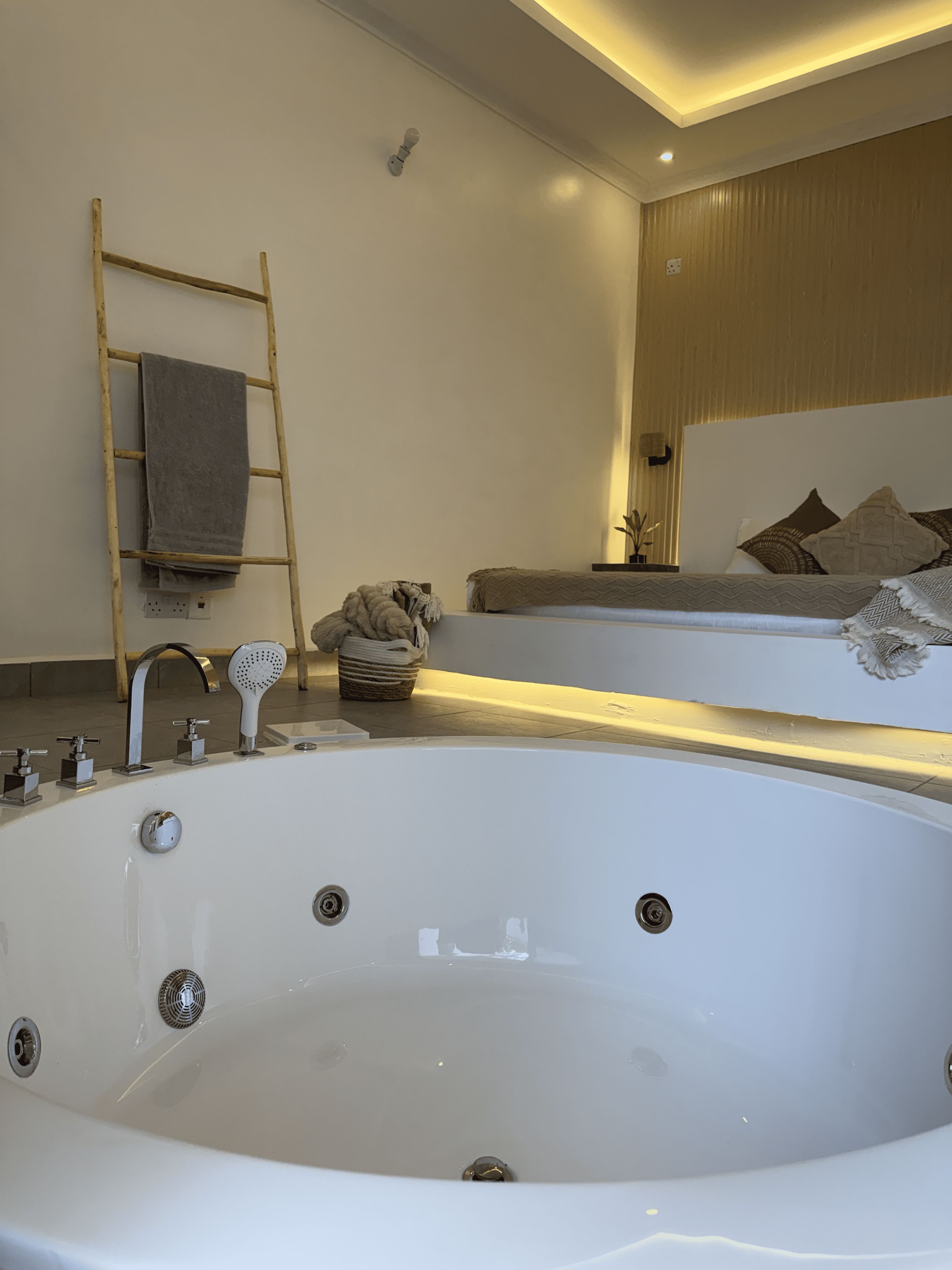 A modern bathroom with a freestanding bathtub, a wooden ladder, and a large mirror above the tub.