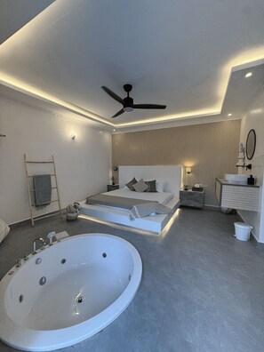 Un dormitorio moderno con una cama grande, una zona de descanso separada, una bañera y un ventilador de techo.