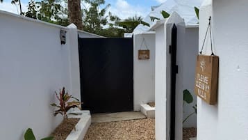 Una entrada protegida con un camino de grava que lleva a un edificio, rodeado de muros blancos y árboles.