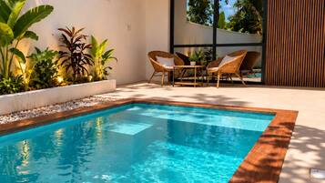 Un área de piscina moderna al aire libre con terraza de madera, sillones de descanso y plantas tropicales.