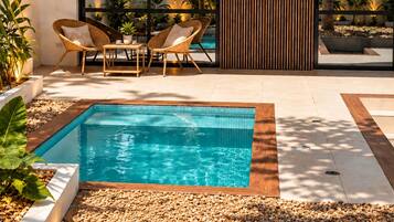 Un área de piscina moderna al aire libre con muelle de madera, mobiliario y vistas al entorno verde.