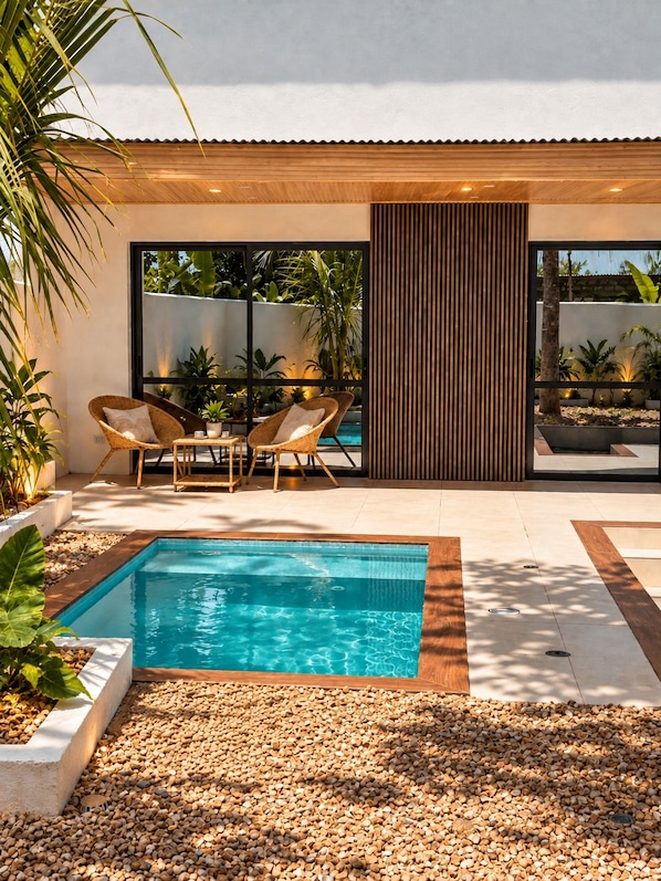 A modern outdoor pool area with a wooden deck, seating, and a view of the surrounding greenery.