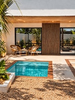 Un área de piscina moderna al aire libre con muelle de madera, mobiliario y vistas al entorno verde.