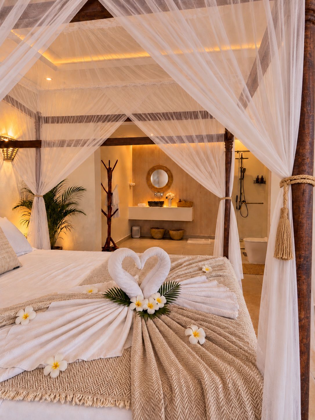 A four-poster canopy bed with a heart-shaped towel centerpiece, a mirror, and a bathroom visible through the canopy.