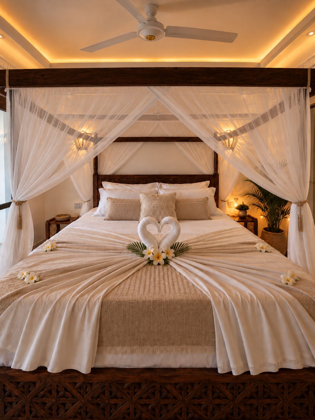 Un dormitorio con cama con dosel, ventilador de techo y un arreglo decorativo de flores y cisnes sobre la cama.