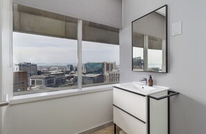 A bathroom with a large window, a white sink, and a mirror. - Central CBD Apartment | Beautiful Views (Cape Town)