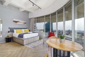 A modern bedroom with a bed, bedside table, and a view of the city through large windows. - Central CBD Apartment | Beautiful Views (Cape Town)