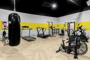 Ett gym med olika typer av träningsutrustning, inklusive löpband, en boxningssäck och styrketräningsmaskiner.