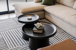 Ein modernes Wohnzimmer mit einer Couch, zwei schwarzen Beistelltischen und einem gemusterten Teppich.