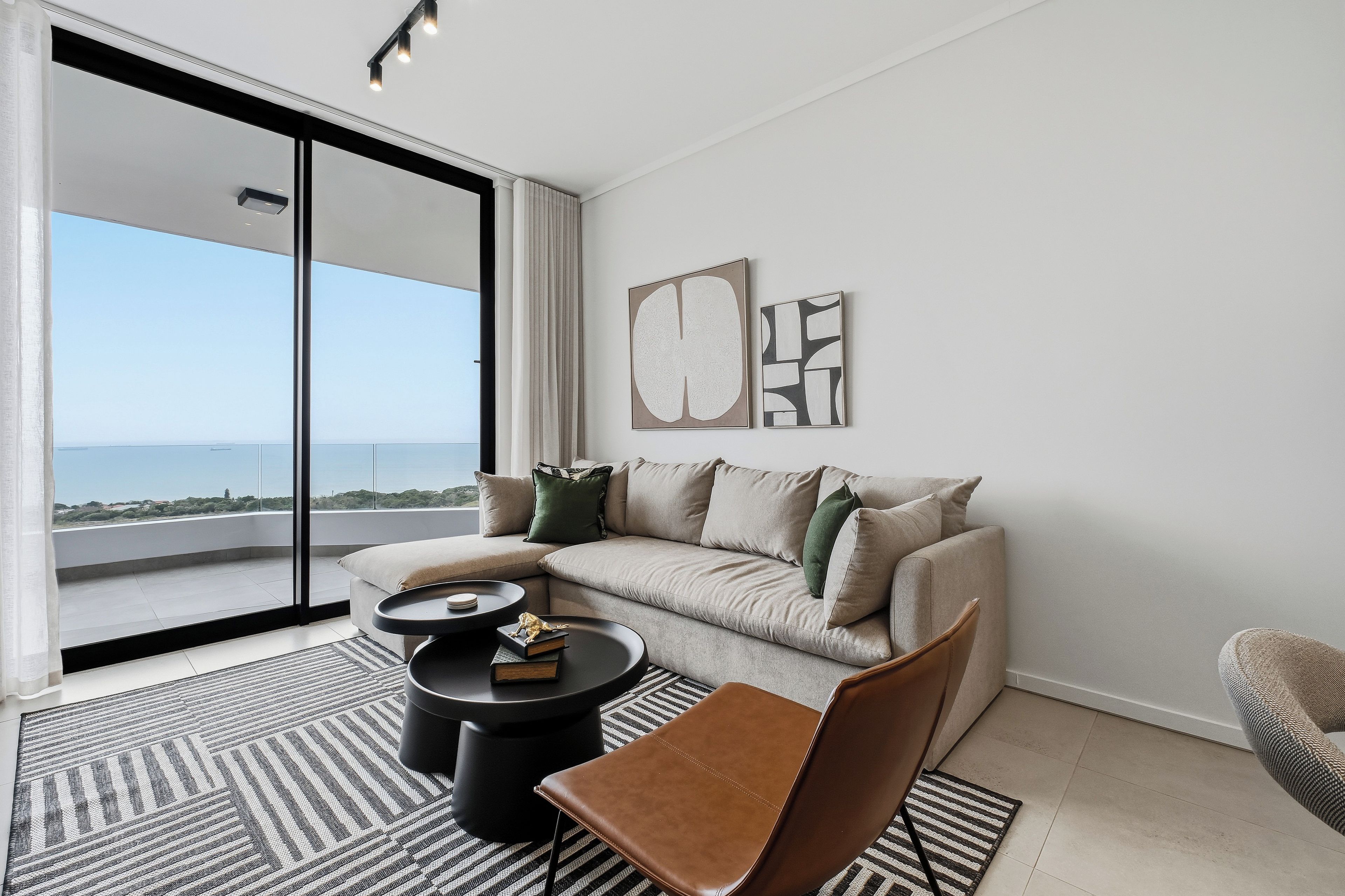 Una sala de estar moderna con un sofá, una mesa de centro y una silla. Hay un ventanal con vista al mar.