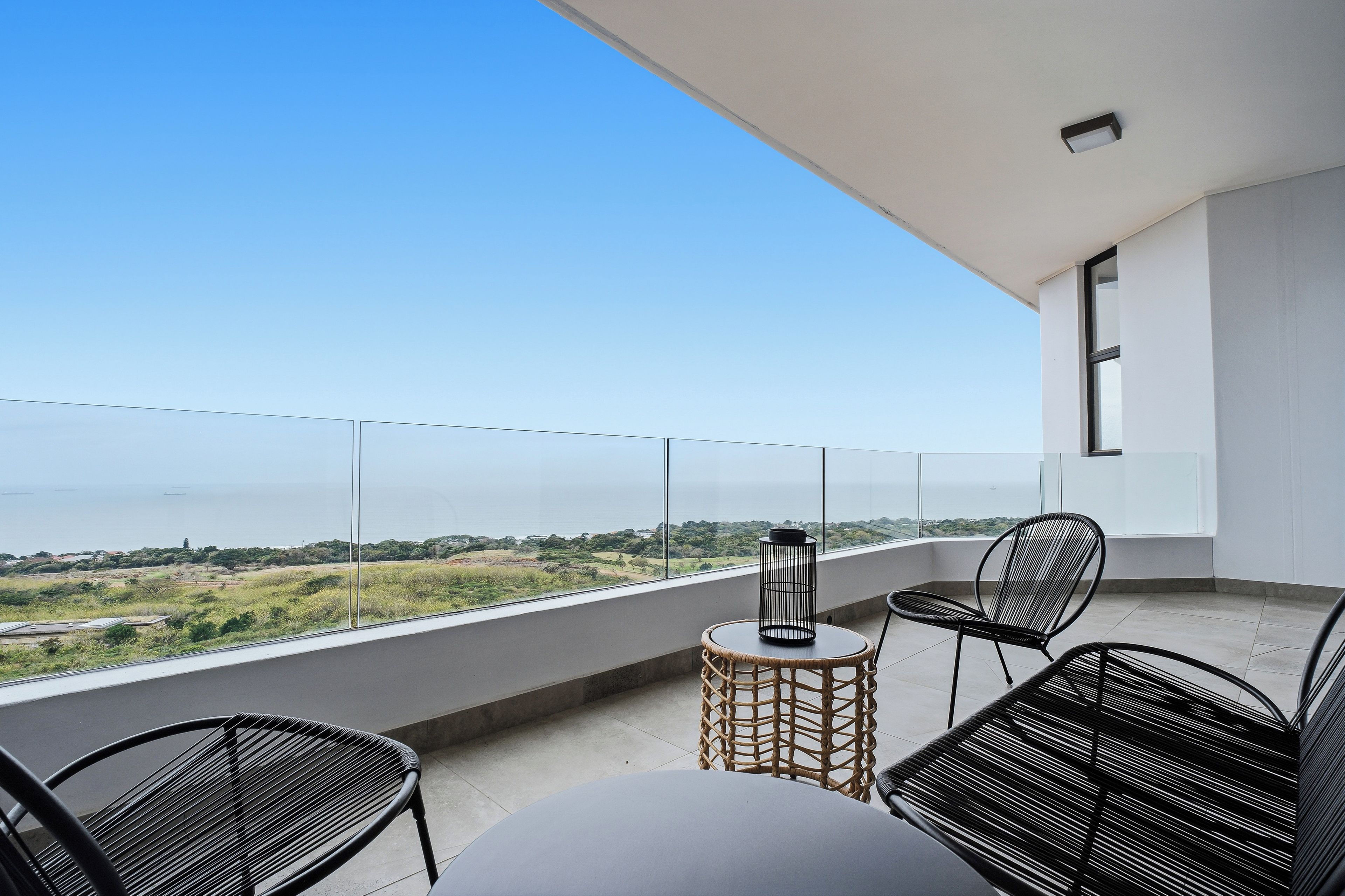Un balcón con vistas al mar, que incluye una mesa redonda, dos sillas y una lámpara de pie.