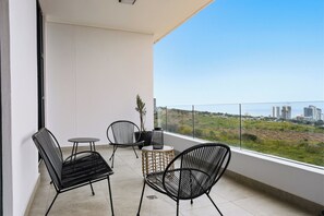 Ein Balkon mit zwei schwarzen Stuhlgestellen aus Drahtgitter, einem kleinen runden Tisch und einem Blumentopf.
