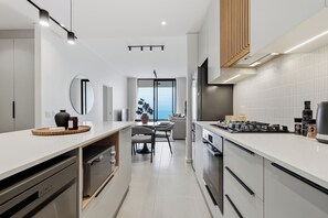 A modern kitchen with white cabinetry, a built-in oven, and a dining area with a table and chairs. - Ocean Vistas | Modern 2BR York | Aircon (Umhlanga)