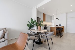 A modern kitchen with a central island, a dining area with a round table and chairs, and a living space with a sofa and a coffee table. - Ocean Vistas | Modern 2BR York | Aircon (Umhlanga)