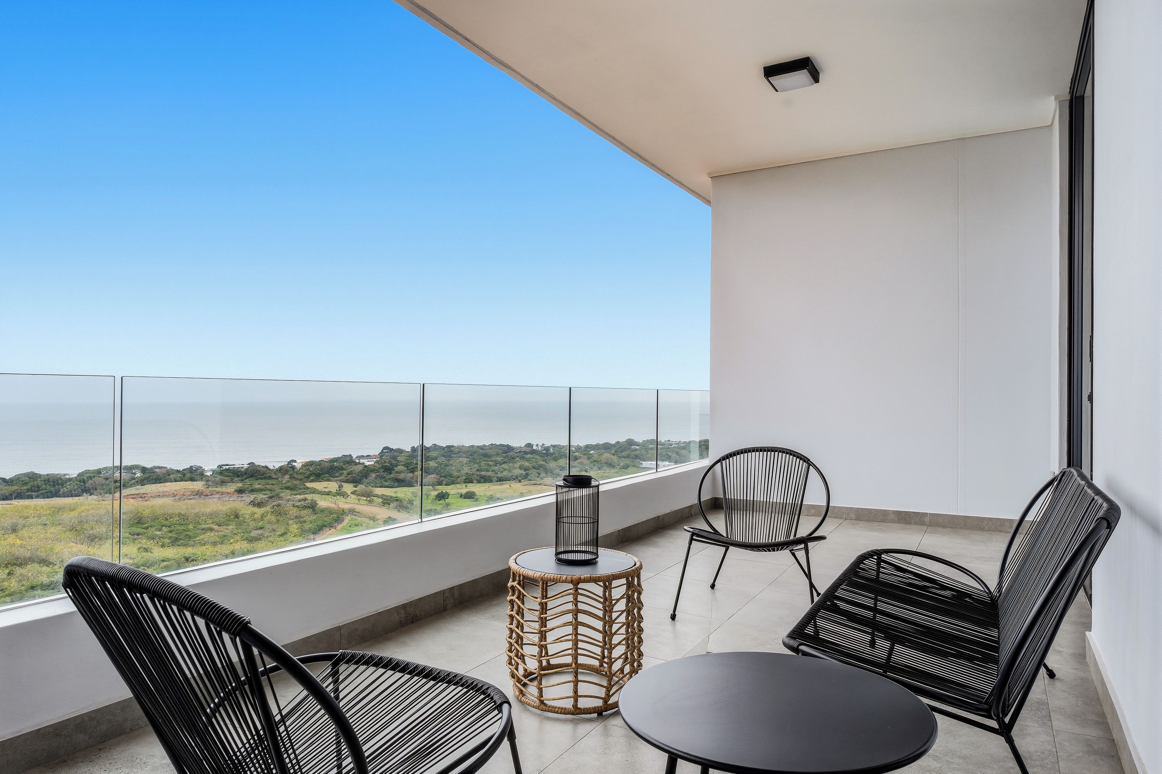 A balcony with a view of the sea, furnished with wicker chairs and a small round table.