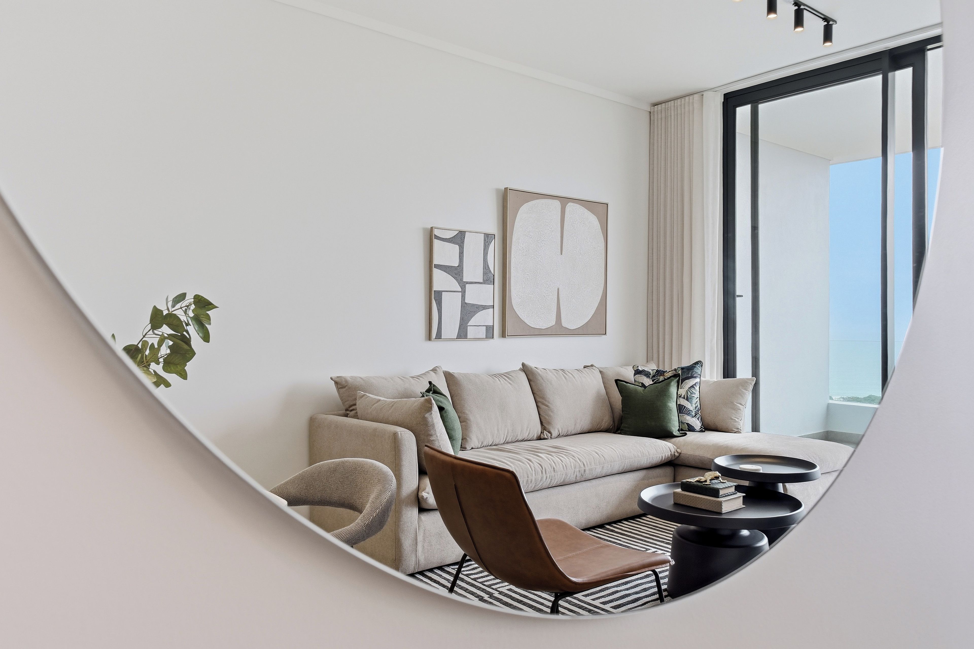 A modern living room with a sofa, armchair, and coffee table, featuring artwork and a large window.