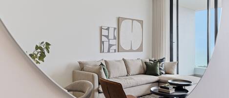 A modern living room with a sofa, armchair, and coffee table, featuring artwork and a large window.