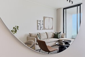 A modern living room with a sofa, armchair, and coffee table, featuring artwork and a large window. - Ocean Vistas | Modern 2BR York | Aircon (Umhlanga)