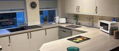 A modern kitchen with a sink, countertop, cabinets, a clock, and a microwave.
