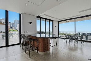 A modern dining area with a central bar, large windows, and a view of the cityscape. - Ocean-View 2BR at The York | Balcony (Umhlanga)