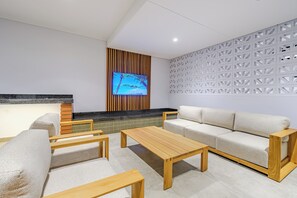 A modern lounge area with a sofa, chairs, a wooden table, a TV screen, and a patterned wall. - Ocean-View 2BR at The York | Balcony (Umhlanga)