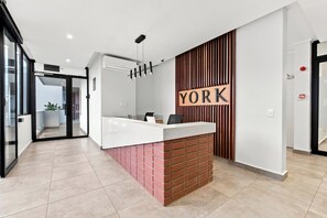 A reception desk with a modern design, a sign that reads 'YORK', and a view of the outside through a glass door. - Ocean-View 2BR at The York | Balcony (Umhlanga)