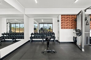 Academia com equipamento de musculação, um espelho grande e vista para o exterior.