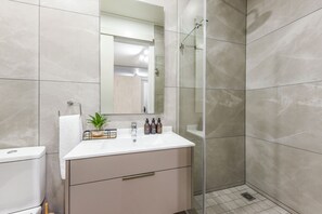 A modern bathroom with a white vanity, a glass shower enclosure, and a mirror above the sink. - Refined City Living with a Contemporary Soul (Johannesburg)