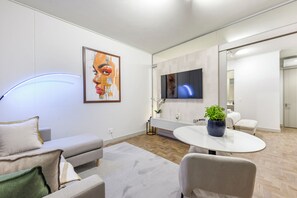 A modern living room with a sofa, a round table with a potted plant, a flat-screen TV mounted on the wall, and a large painting. - Refined City Living with a Contemporary Soul (Johannesburg)