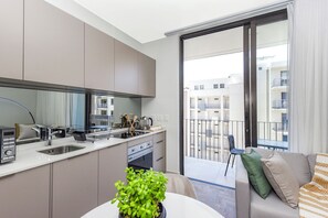 A modern kitchen with a built-in oven, a dining area with a table and chairs, and a balcony with a view of the surrounding buildings. - Refined City Living with a Contemporary Soul (Johannesburg)