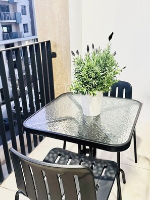 A balcony with a glass table and two chairs, a potted plant, and a view of a building. - Refined City Living with a Contemporary Soul (Johannesburg)