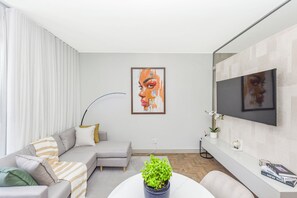 Un salon moderne avec un canapé gris, une table basse agrémentée d’une plante, un tableau accroché au mur et un téléviseur à écran plat fixé au mur.
