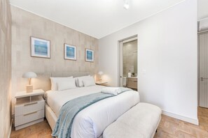 Une chambre à coucher moderne, comprenant un lit, des tables de chevet, un banc et des œuvres d’art accrochées au mur.