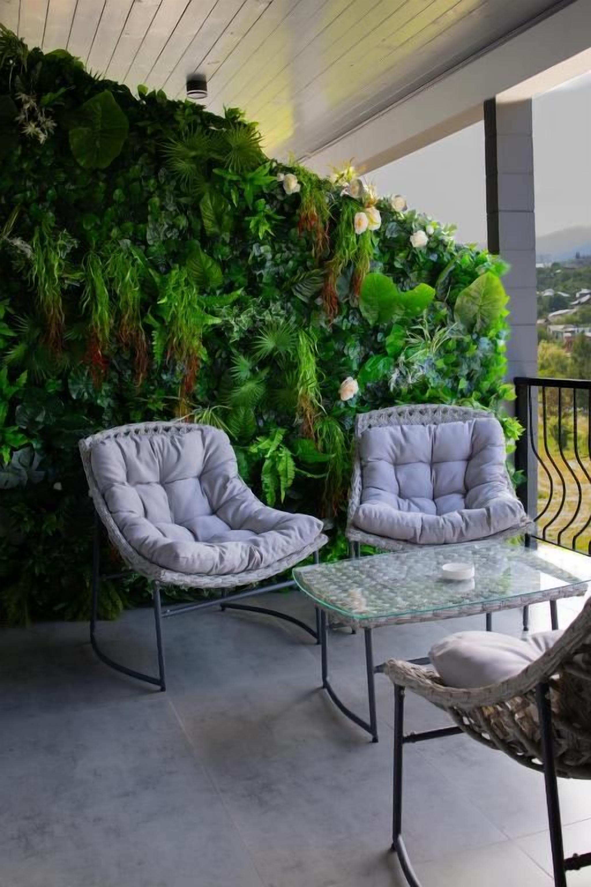 Varanda com duas cadeiras estofadas, uma mesa de vidro e um painel de parede verde e exuberante.