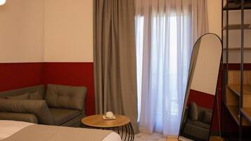 Habitación de hotel con cama, sofá, una pequeña mesa redonda con un control remoto, un espejo grande y una estantería.