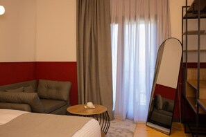 Ein Hotelzimmer mit einem Bett, einer Couch, einem kleinen runden Tisch mit einer Fernbedienung, einem großen Spiegel und einem Bücherregal.
