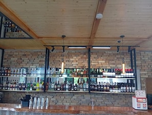 A bar area with wooden ceiling beams, brick walls, and shelves stocked with various bottles.