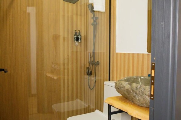 Une douche avec une porte en verre, un mur en bois et un lavabo en pierre posé sur une étagère en bois.